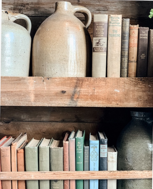 A bookcase holding antique books and old stoneware jugs.