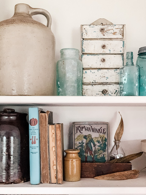 a shelf full of vintage goodies such as books and mason jars and stoneware