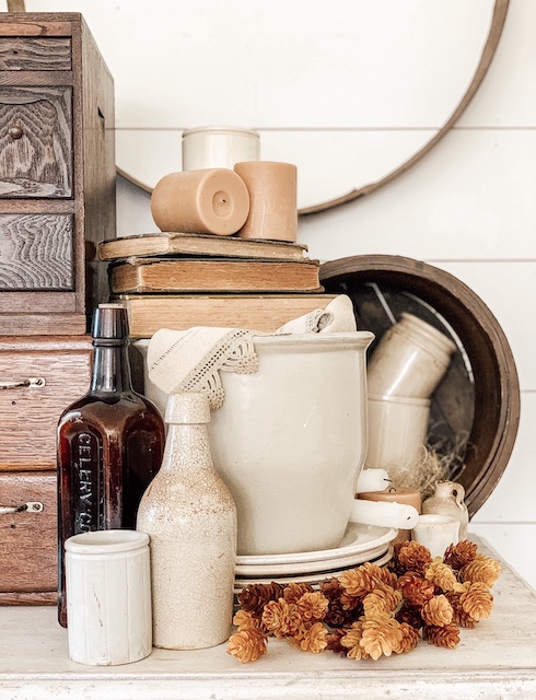 A fall vignette filled with stoneware, fall flowers, old books, and an amber bottle.  