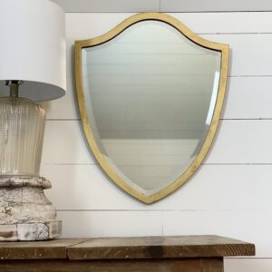 Gold mirror hanging on a wall beside a lamp and above a table