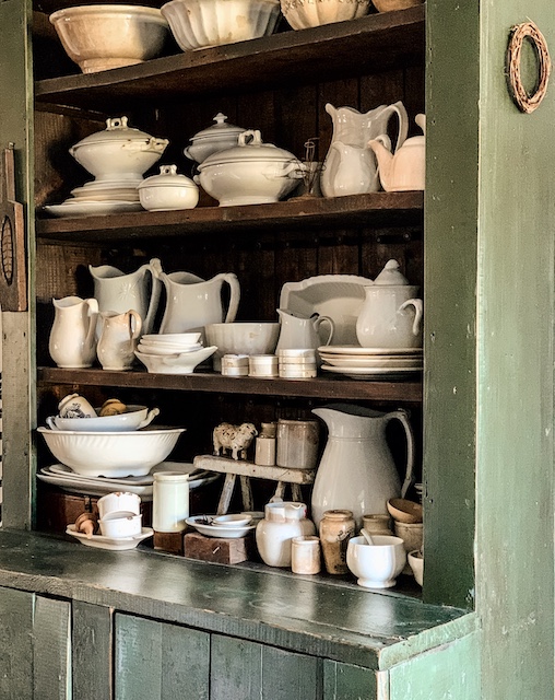 An old green stepback cupboard full of old dishes.
