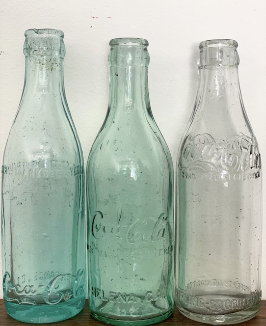 Three old straight edge coke bottles sitting on a table.