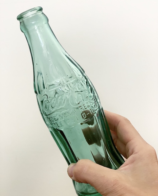 A man holding an old coke bottle trying to date it.