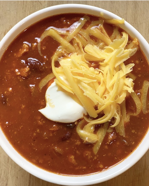 a big bowl of chili with sour cream and shredded cheese on top