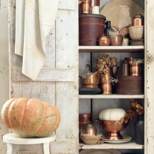 A chippy white cabinet filled with vintage copper for fall decor.