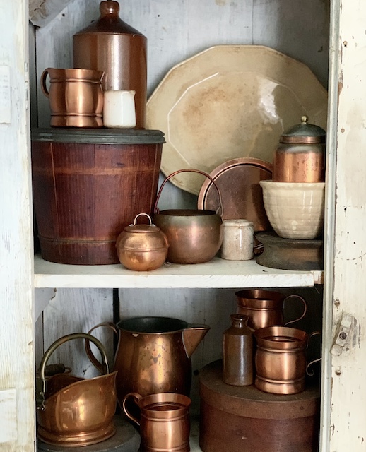 A set of white shelves with brown boxes, copper and ironstone.