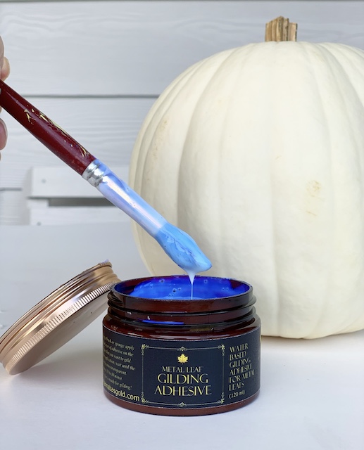 a paint brush being dipped into adhesive about to be allied onto a pumpkin

