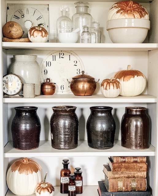 A bookcase of vintage items and copper guilded pumkins.
