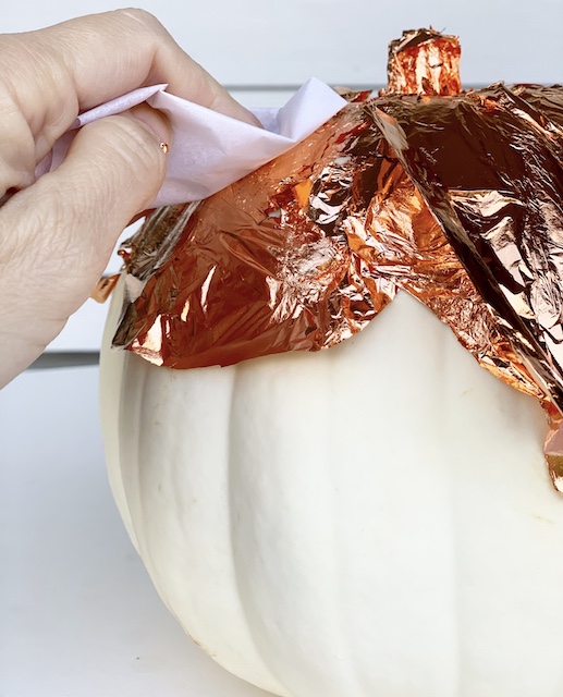 Using a piece of tissue, pushing down on a piece of gilding leaf onto a pumpkin.