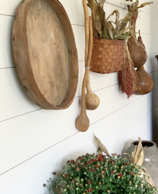 A white peg rail with fall items hanging from it with a mum below it