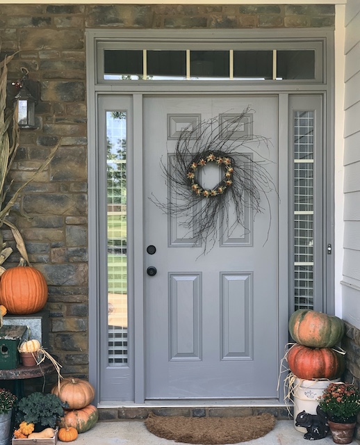 A front door with a fall wreath hanging in it.