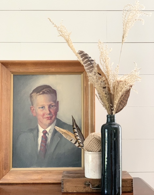 Feathers and pampas grass in a vase next to a portrait for decor