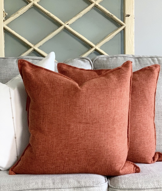 Two burnt orange pillows sitting on a sofa for fall decor.