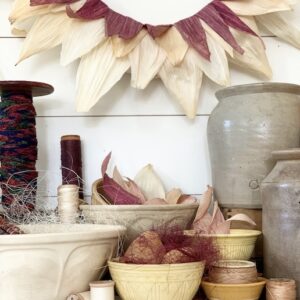 a corn husk wreath with pops of purple on the wall.