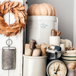 A fall set up filled with crocks and pumpkins and rolling pins and other old kitchen items.