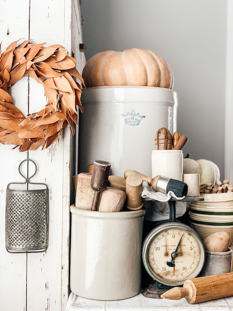 A fall set up filled with crocks and pumpkins and rolling pins and other old kitchen items.