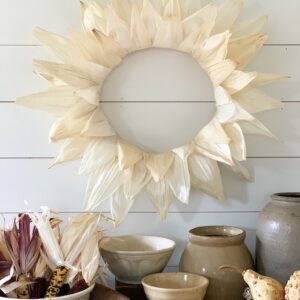 a corn husk wreath on a wall with bowls under for fall