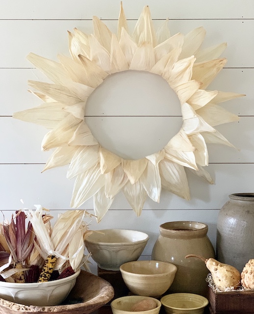 a corn husk wreath on a wall with bowls under for fall