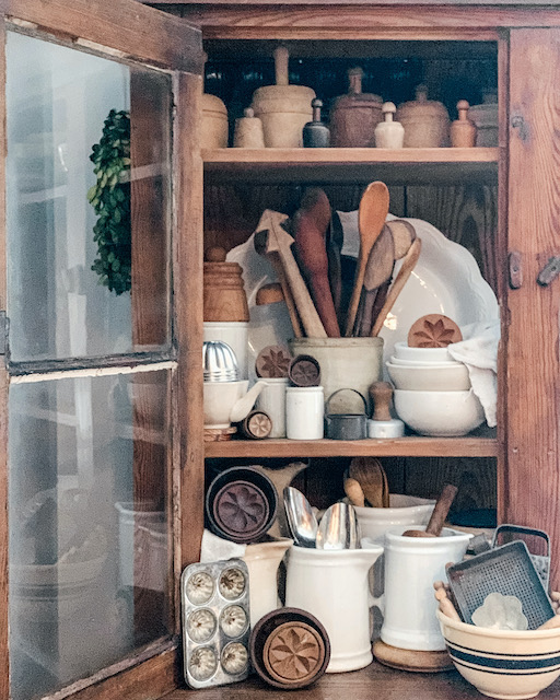 a wide shot of a cabinet filled with wooden butter molds and lots of other old kitchen goodies