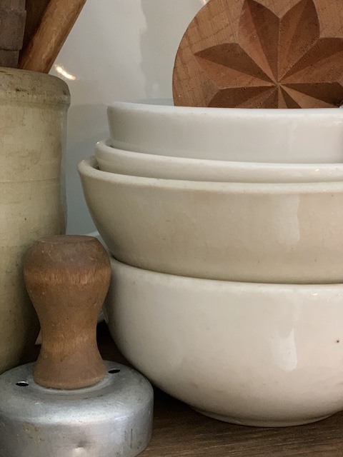 a wooden butter mold sitting in a stack of old ironstone bowls