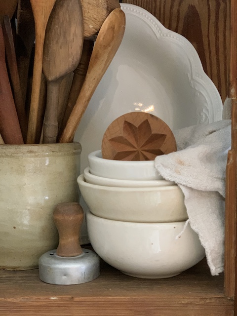a grouping of old spoons stuffed in a crock and old bowls as decor with a butter mold in it