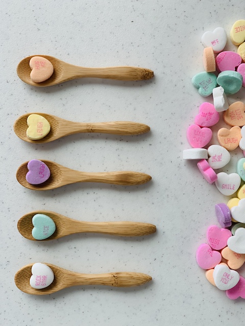 a single conversation heart in a spoon with a pile of them around
