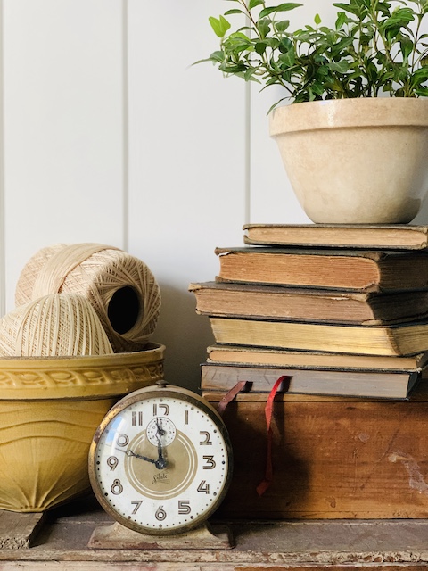 a vintage display with a bowl and a clock and some books and some yarn