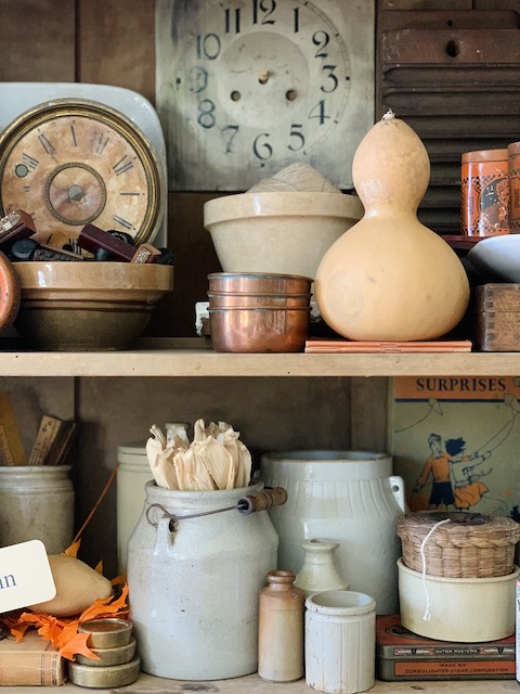 gourd and clock face and crocks all styled on the shelf