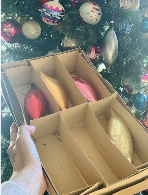 holding a box and reaching for an ornament off the tree