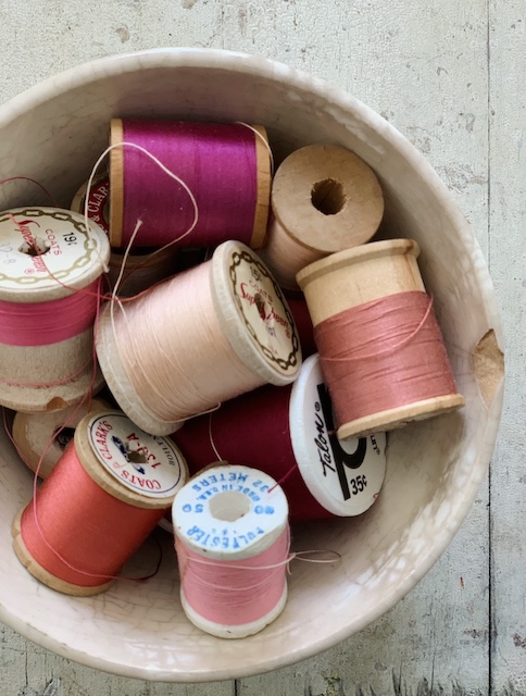 A bowl full of red and pink thread spools